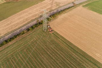 Bauer mit seinem Traktor bei der Grasernte am Fuße eines Strommasten