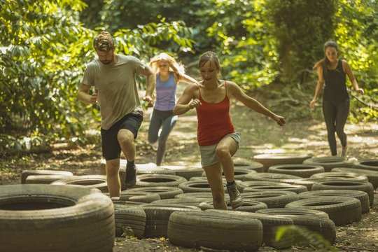 Group of people running over tires during obstacle course - Powered by Adobe