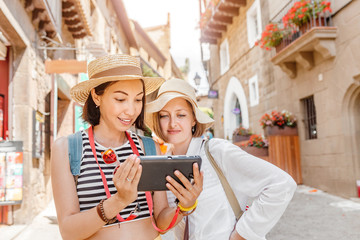 vacation and travel concept - two beautiful girls toursits looking into tablet pc in the old city...