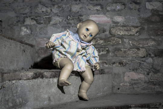 Scary demonic doll sitting on the steps in the basement