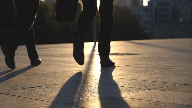Feet of two businessmen walking in city street with sun flare at background. Business men commute to work together. Confident guys being on his way to office. Colleagues going outdoor. Slow motion