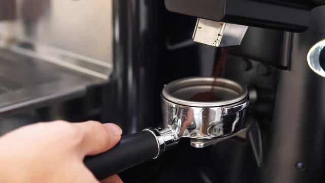 Barista holding portafilter getting ground coffee from automatic grinder machine