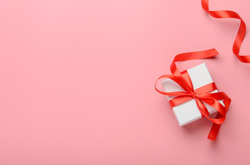 White gift box with a red bright ribbon on pink background. A gift for the new year, Christmas,...
