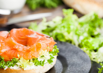 Fresh healthy bagel sandwich with salmon, ricotta and lettuce on black plate on black kitchen table background. Healthy diet food. Glass of milk and fresh vegetables