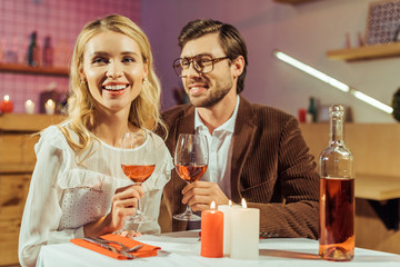 laughing couple with wine glasses celebrating and having date at table with candles in restaurant