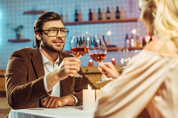 selective focus of young couple celebrating and clinking by wine glasses at table with candles in restaurant