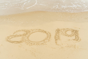 2019 written on sandy beach with wave approaching.