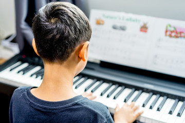 asian kid boy  playing the piano in the room