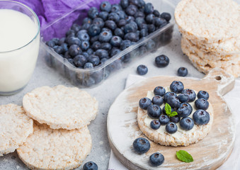 Healthy organic rice cakes with ricotta and fresh blueberries and glass of milk on light stone kitchen background. Top view. Plastic tray of strawberries