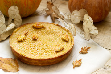 Traditional American pumpkin homemade cake, decorated with cookies on a background of pumpkins and autumn leaves.