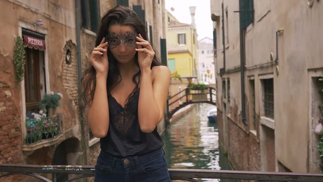 Woman with carnival mask in Venice. Attractive young sensual romantic woman standing on the bridge against beautiful view on venetian chanal with boats and gondolas in Venice, Italy.