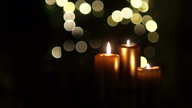 Close up of three burning candles with blurred Christmas light background. In the frame flashes a dark shadow, closing the candles. Mysterious stranger, mysticism, spiritualism