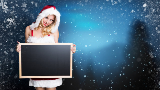 attractive miss santa with an empty blackboard in a snowy landscape