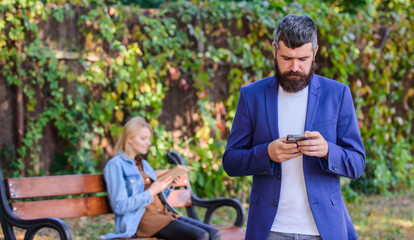Man with beard hold smartphone while girl sit bench park. Man use application for dating. Guy...