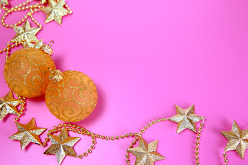 Two yellow shiny glass balls and necklace of golden stars for Christmas decoration on the pink background. Christmas and New Year holiday background concept. Copy space for text.