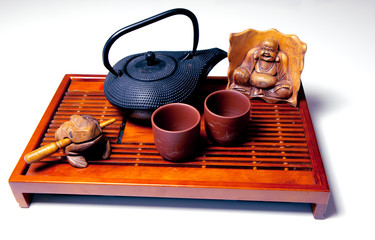 Metal black teapot, two cups of tea, Hotei and frog wooden statuettes on the traditional wooden tea table. White background.