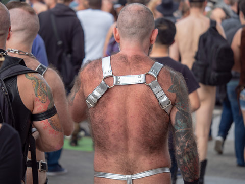 Rear view of hairy man wearing silver BDSM harness and thong walking in cro...