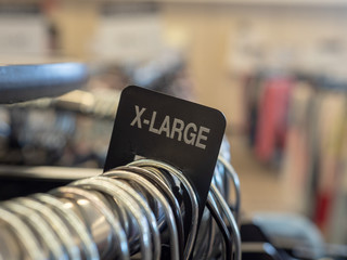 X-large extra large clothes section sign on steel hanging rack with hangers in department store