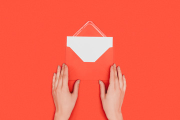 cropped shot of person opening envelope with card isolated on red