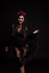 Portrait of a girl in the image for Halloween. Black Widow. Wreath of roses. Makeup for halloween. Holds a dress. Black transparent lace dress. Black background.
