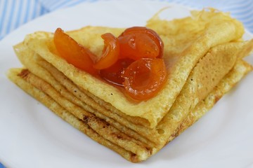 Delicious hot pancakes with apricot jam on a white plate.