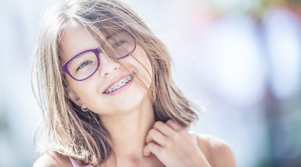 Fototapeta premium Happy smiling girl with dental braces and glasses. Young cute caucasian blond girl wearing teeth braces and glasses
