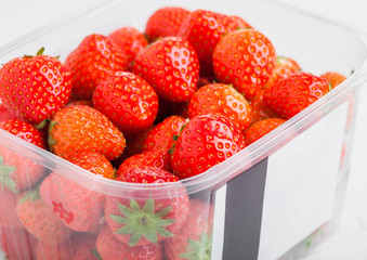 Plastic tray container of fresh organic healthy strawberries on stone kitchen table background. Tray with label