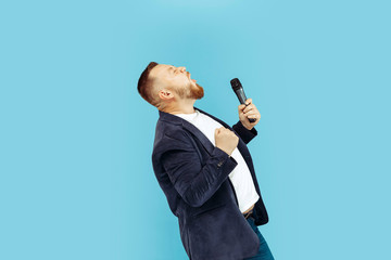 Young man with microphone on blue studio background, leading concept. Human emotions and facial expressions concepts.