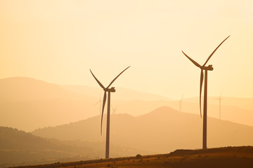Obraz premium Wind power generators on the background of silhouettes of mountain peaks. Simplicity and minimal lines. Beautiful landscape of the power of nature. 