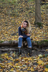 Young beautiful girl with long hair, with a scarf around his neck, sits on a log of fallen tree in the autumn forest among fallen yellow leaves