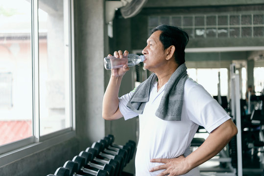 Asian Senior Man Thirsty Drinking Water After Exercise In Fitness Gym. Elderly Healthy Lifestyle.