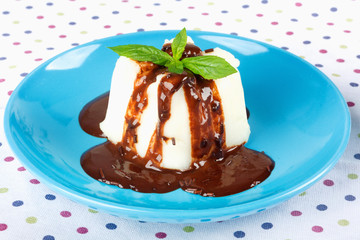 Cream pudding with chocolate sauce and mint on  multicolored tablecloth.