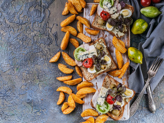Appetizing toasts with avocado, quail eggs, tomatoes, Dor Blue cheese and french fries. Author's...