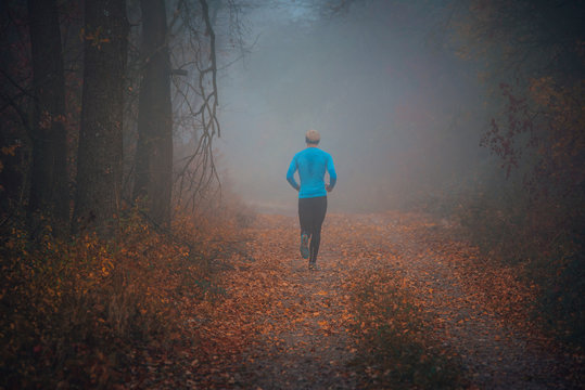 Trail runner run in misty autumn forest