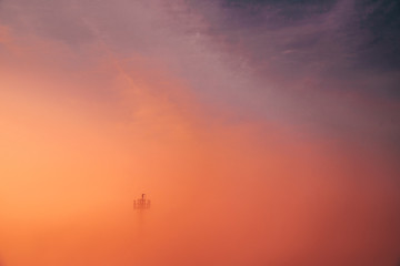 Fototapeta na wymiar Adventure photo. Man at the top of tower in colorful morning mist. Orange edit space