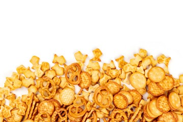 A photo of an assortment of salt crackers, sticks, pretzels, and fishes, shot from the top on a white background with copy space. Party snacks mix