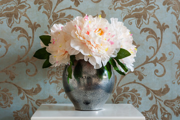 A bouquet of peonies in a metal vase on the bedside table in the bedroom