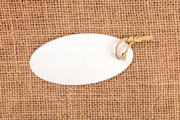 A photo of a white paper label or a price tag, shot from the top on a rustic burlap background with...