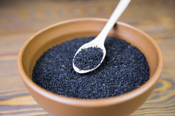 Black cumin (nigella sativa or kalonji) seeds in spoon on wooden background, selective focus
