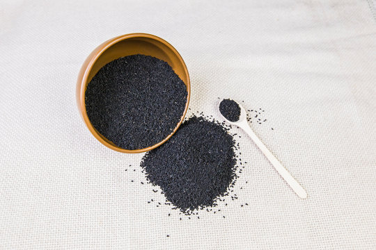 Black cumin in a plate with a wooden spoon on a light burlap background