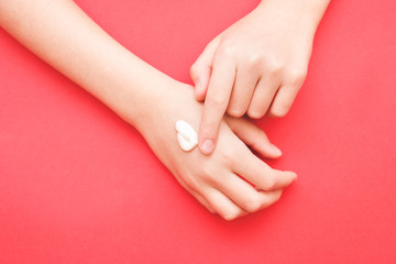 the woman's hand smeared her hand with cosmetic cream lotion with a copy of space on a red background of minimalism. The concept of women's pattern blog