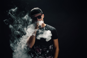 Vape man. Portrait of a handsome young white guy in a modern black cap vaping and letting off puffs...