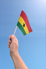 Hand holding Ghana flag high in the air, with a clear blue sky