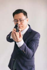 Asian businessman aiming with a gun.