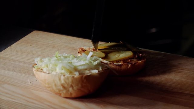 Chef making burger. frying the bun on the grill, putting sliced pickled cucumber