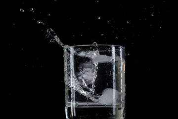 Bounce and splash from a piece of ice thrown into a transparent glass with water on a black background