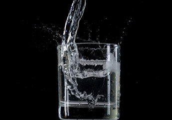 Bounce and splash from a piece of ice thrown into a transparent glass with water on a black background