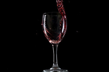 Red wine falls into a glass and creates splash and splashes on a black background.