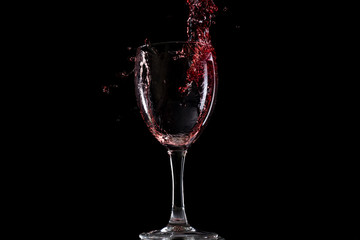 Red wine falls into a glass and creates splash and splashes on a black background.