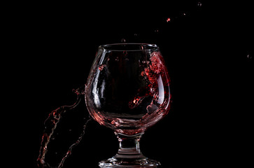 Naklejka na ściany i meble Red wine falls into a glass and creates splash and splashes on a black background.